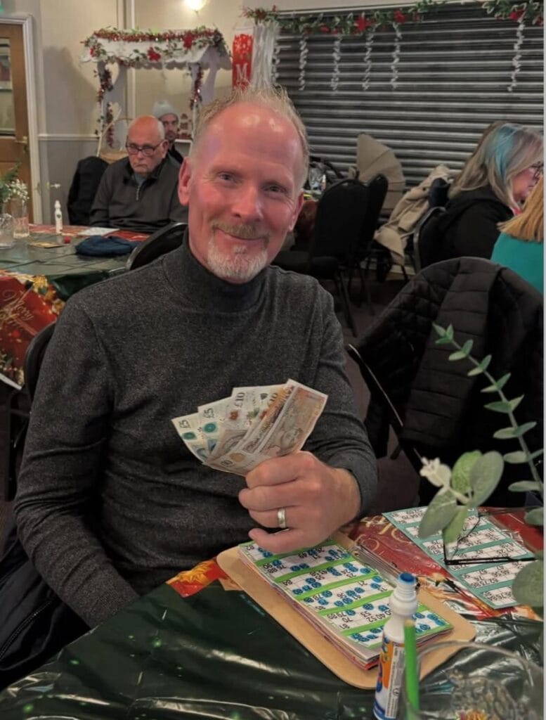 Man smiling while holding British banknotes at bingo table.