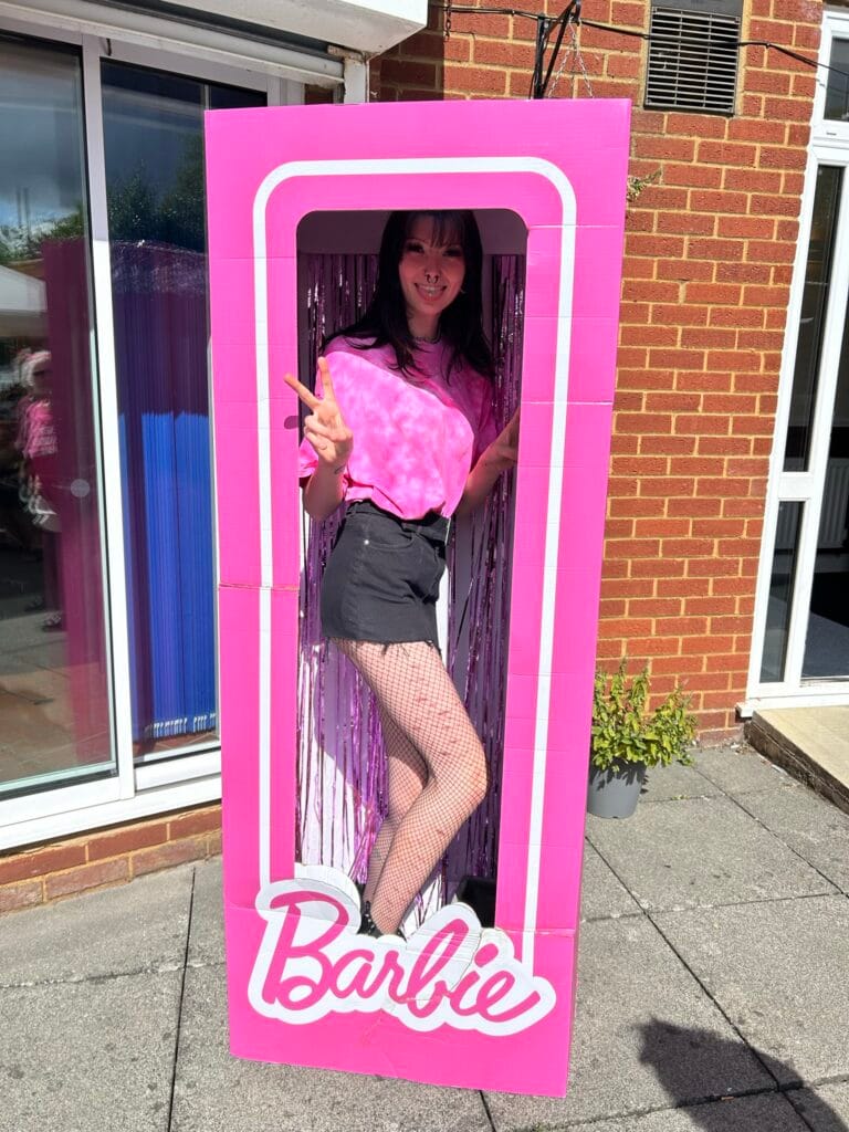 Person posing inside pink Barbie photo box outdoors