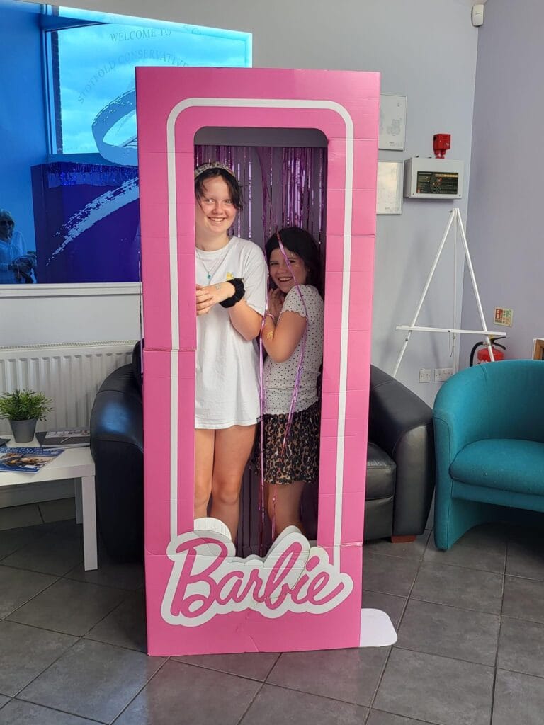 Two girls posing inside pink Barbie photo frame